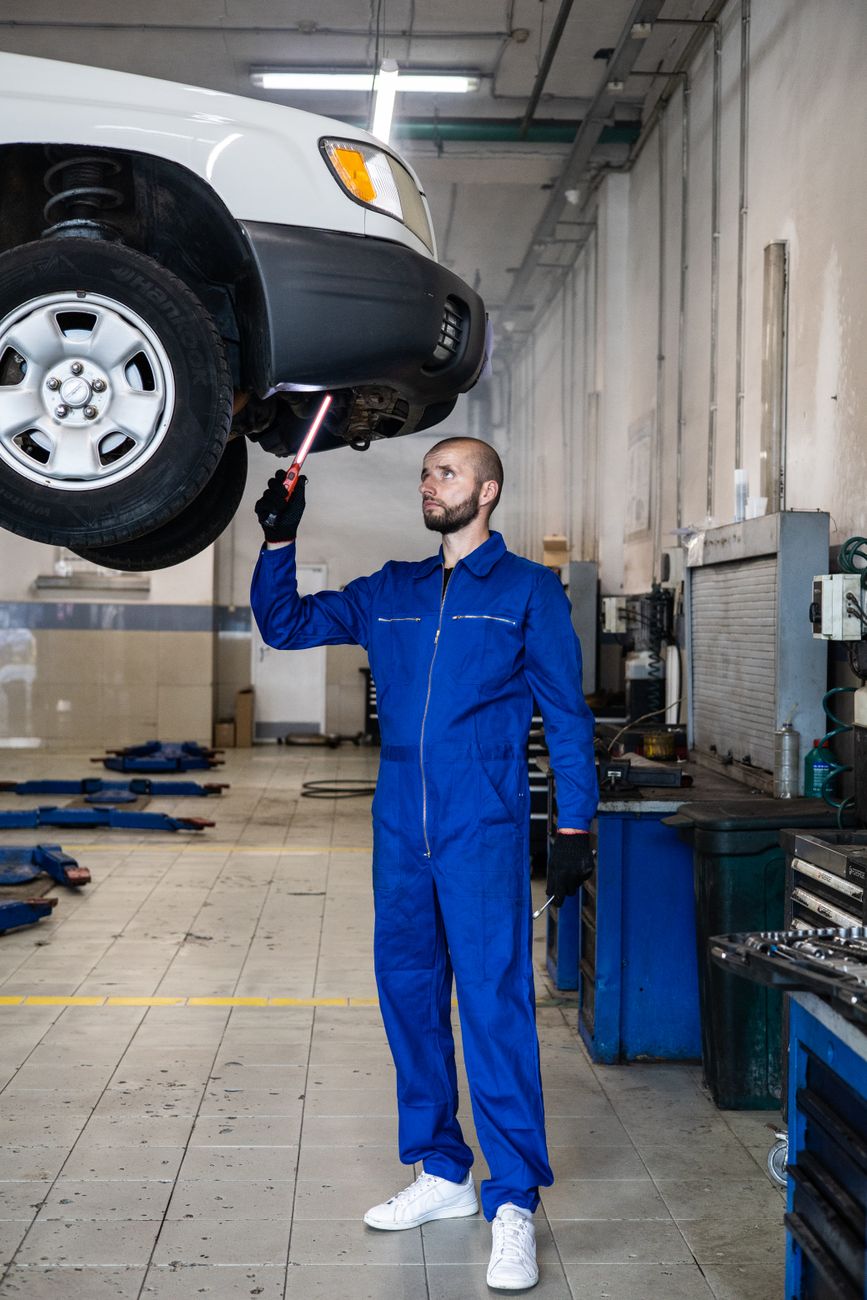 Mechanic in blue coveralls inspecting a car in the repair bay